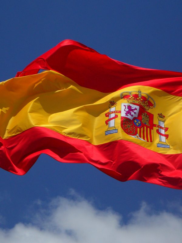 A Spanish flag waving in the wind against a blue sky